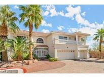 Elegant two-story home with a balcony, arched windows and mature palm trees at 7682 Calm Passage Ct, Las Vegas, NV 89139
