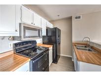 Compact kitchen features white cabinetry, wood countertops, and black appliances at 1381 E University Ave # 204, Las Vegas, NV 89119