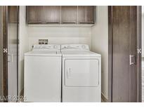 A clean and well-organized laundry area with a white washer and dryer, and upper cabinets for storage at 8925 W Flamingo Rd # 110, Las Vegas, NV 89147