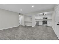 Open living room with gray wood flooring, white walls, and updated kitchen with stainless steel appliances at 5009 Indian River Dr # 153, Las Vegas, NV 89103