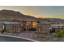 Striking home with a modern design, lush landscaping, and a paver driveway, set against a backdrop of mountains at 10096 Amethyst Hills St, Las Vegas, NV 89148