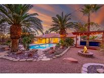 Inviting backyard with pool, fire pit, and covered patio, perfect for outdoor entertaining against a colorful sunset at 1561 Doran Dr, Las Vegas, NV 89123