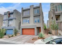 Modern three-story home featuring clean lines, gray stucco, an orange garage door, and low-maintenance landscaping at 8087 Carpenter Creek Ave, Las Vegas, NV 89113