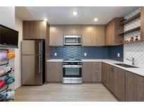 A modern kitchen with stainless steel appliances, wood cabinets, and a blue tile backsplash at 4421 Halbert Ave, Las Vegas, NV 89110