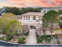 Elegant two-story home featuring lush landscaping, a terracotta roof, and an arched entryway at sunset at 9325 Verlaine Ct, Las Vegas, NV 89145