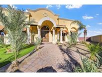 Stunning front of house features a yellow stucco exterior, arched entry, columns, and a paved walkway and well landscaped yard at 6760 Hinson St, Las Vegas, NV 89118