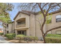 Exterior view of tan condo building with balconies, landscaped shrubs and gravel, set against a blue sky at 8250 N Grand Canyon Dr # 2102, Las Vegas, NV 89166