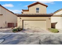 Tan home featuring a two-car garage with a brick paver driveway and well-maintained desert landscaping at 7059 Mackenzie Bay Ave, Las Vegas, NV 89179