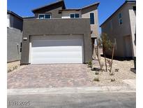 Contemporary two-story home with a gray facade, white garage door, and brick paved driveway at 10012 River Corral St, Las Vegas, NV 89166