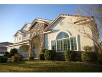 Charming stucco home with a stone archway, well-manicured lawn, and a beautiful landscape at 7444 Grassy Field Ct, Las Vegas, NV 89131