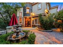 Beautiful two-story home featuring stone accents, a water fountain, mature landscaping, and a decorative entryway with double doors at 801 Sir James Bridge Way, Las Vegas, NV 89145