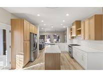 Bright, open kitchen features stainless steel appliances, center island with white countertops and light wood cabinets at 3110 Scotts Valley Dr, Henderson, NV 89052