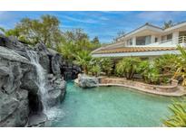 Beautiful backyard pool featuring a rock waterfall and lush tropical landscaping at 2221 S Tioga Way, Las Vegas, NV 89117