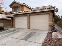 Beige two-car garage with a concrete driveway and desert landscaping featuring shrubs and rock at 8009 Draco Cir # 201, Las Vegas, NV 89128