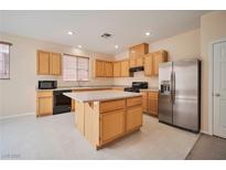 Bright kitchen features an island, stainless steel refrigerator, and natural wood cabinetry at 7317 Caballo Range Ave, Las Vegas, NV 89179