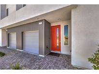 Modern home featuring a gray exterior, two-car garage, brick paver driveway, and a vibrant orange front door at 8629 Ensworth St # 113, Las Vegas, NV 89123