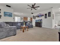Inviting living room with a large gray sectional, neutral carpet, and an open floor plan to the kitchen at 4211 Enchanting Sky Ave, North Las Vegas, NV 89081