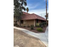 A tan one-story townhome with a red tile roof and mature trees at 2425 Paradise Village Way, Las Vegas, NV 89120