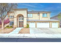 Beige two-story home with a three-car garage, arched entryway, and desert landscaping at 694 Tomscott Ave, Henderson, NV 89052