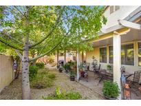 A view of the backyard with a covered patio and desert landscaping featuring mature shade trees at 7172 Painted Paradise St, Las Vegas, NV 89131