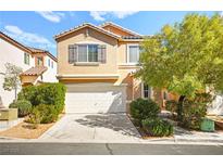 Two-story tan home featuring a two-car garage, green bushes and a mature tree in the front yard on a sunny day at 3920 Beverly Elms St, Las Vegas, NV 89129