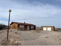 Rustic wooden home with boarded-up windows, situated on a gravel lot under a cloudy sky at 895 Greasewood Ln, Moapa, NV 89025