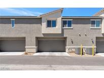 Exterior view of a townhome featuring garages and beige stucco under a bright blue sky at 12367 Indigo Montage Rd # 3, Las Vegas, NV 89183
