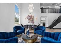 Bright living room features high ceilings, staircase, modern lighting and comfortable blue velvet seating area with a chess table at 9417 Churchill Downs Dr, Las Vegas, NV 89117