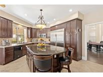 Bright kitchen features a granite island, stainless steel refrigerator, dark wood cabinets, and elegant chandelier at 9517 Spanish Steps Ln, Las Vegas, NV 89117
