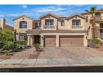 Two-story tan home featuring a tile roof, balcony, paver driveway and a two-car garage with arched windows at 9967 Pipestone St, Las Vegas, NV 89141