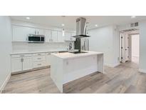 Bright kitchen features white cabinets, stainless steel appliances, island with seating and gray wood floors at 4330 Sandy River Dr # 86, Las Vegas, NV 89103