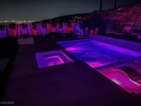 Inviting backyard pool and spa with ambient lighting and views of the city skyline at night at 270 Shaded Canyon Dr, Henderson, NV 89012