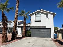 Two-story home featuring a gray garage door, desert landscaping, and palm trees set against a bright blue sky at 6532 Moon Roses Ct, Las Vegas, NV 89108