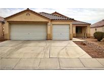 Tan home with a large driveway leading to a two-car garage with a well maintained landscape at 3432 Pastori Valley Ct, North Las Vegas, NV 89032