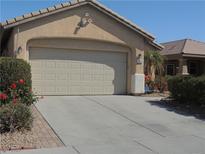 Beige one story home with a two car garage, concrete driveway, and manicured landscaping featuring roses at 6076 Wheat Penny Ave, Las Vegas, NV 89122