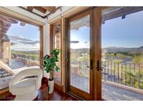 Elegant balcony view with wood floors, glass doors, white chair, and a glimpse of the scenic landscape at 15 Rue Du Rivoli Pl, Henderson, NV 89011