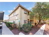 Beige stucco condo building with well maintained bushes and landscaping and a covered parking area on a bright day at 7200 Pirates Cove Rd # 1011, Las Vegas, NV 89145