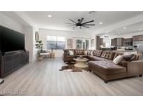 Bright living room with a brown leather sectional sofa, modern ceiling fan, and large flat screen TV at 11913 Alava Ave, Las Vegas, NV 89138
