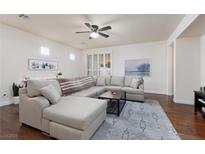 Bright living room features an oversized sectional, ceiling fan, and gorgeous hard wood floors at 3239 Robins Creek Pl, Las Vegas, NV 89135