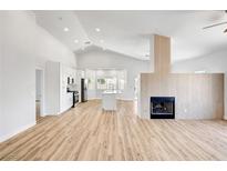 Open-concept living room featuring a modern fireplace and adjacent kitchen with sleek white cabinets at 689 Hitchen Post Dr, Henderson, NV 89011