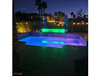 A backyard pool and waterfall feature illuminated by color-changing LED lights offers a relaxing outdoor retreat at night at 8209 Chapelle Ct, Las Vegas, NV 89131