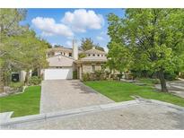 Beautiful home featuring a circular stone facade, green lawn, and brick driveway at 12056 Royal Dolnoch Ct, Las Vegas, NV 89141