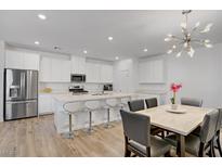 Bright kitchen features an island with seating, stainless steel appliances, and a dining area with modern light fixture at 4436 Mural Glen Ct, North Las Vegas, NV 89084
