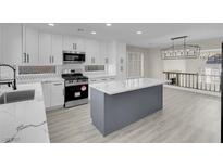 Modern kitchen features white cabinets, stainless steel appliances, and a gray kitchen island with marble countertops at 8232 Ocean Terrace Way, Las Vegas, NV 89128