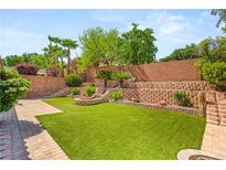 Expansive backyard features lush green turf, tiered retaining walls, and a charming stone fire pit at 11764 Golden Moments Ave, Las Vegas, NV 89138