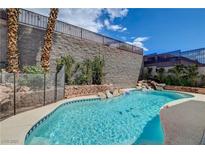 Beautiful in-ground pool with waterfall feature, stone accents, and secure fencing for safety at 2078 Wildwood Lake St, Henderson, NV 89052
