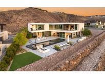 Modern home featuring a sleek pool, fire pit, and expansive glass walls against a mountainous backdrop at 13 Rockstream Dr, Henderson, NV 89012