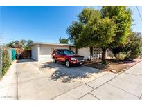 Charming single-story home featuring a large driveway, mature tree, and a red SUV parked out front on a sunny day at 2600 E Owens Ave, North Las Vegas, NV 89030