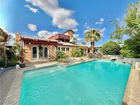 A sparkling pool with a tanning ledge is surrounded by a patio and lush greenery at 107 Elm St, Henderson, NV 89015