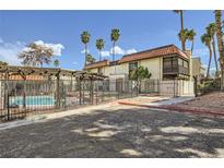 View of community pool and residential building with tropical landscaping and an iron fence on a bright day at 1420 Vegas Valley Dr # 22, Las Vegas, NV 89169